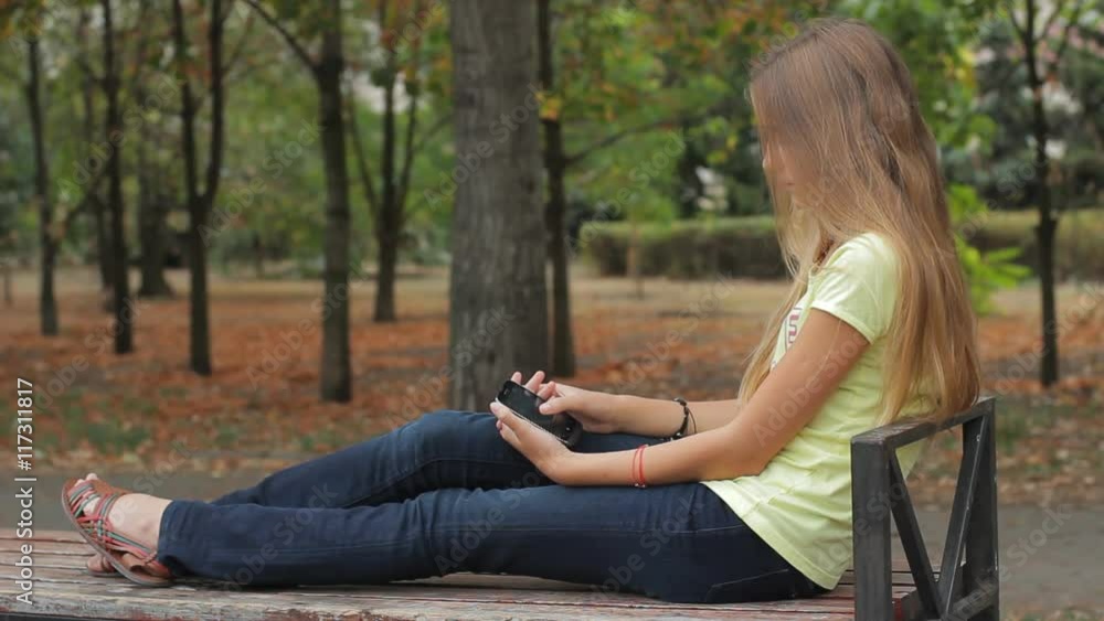 Sad teen girl with smartphone sitting on park bench Sad teen girl with smartphone sitting on park bench