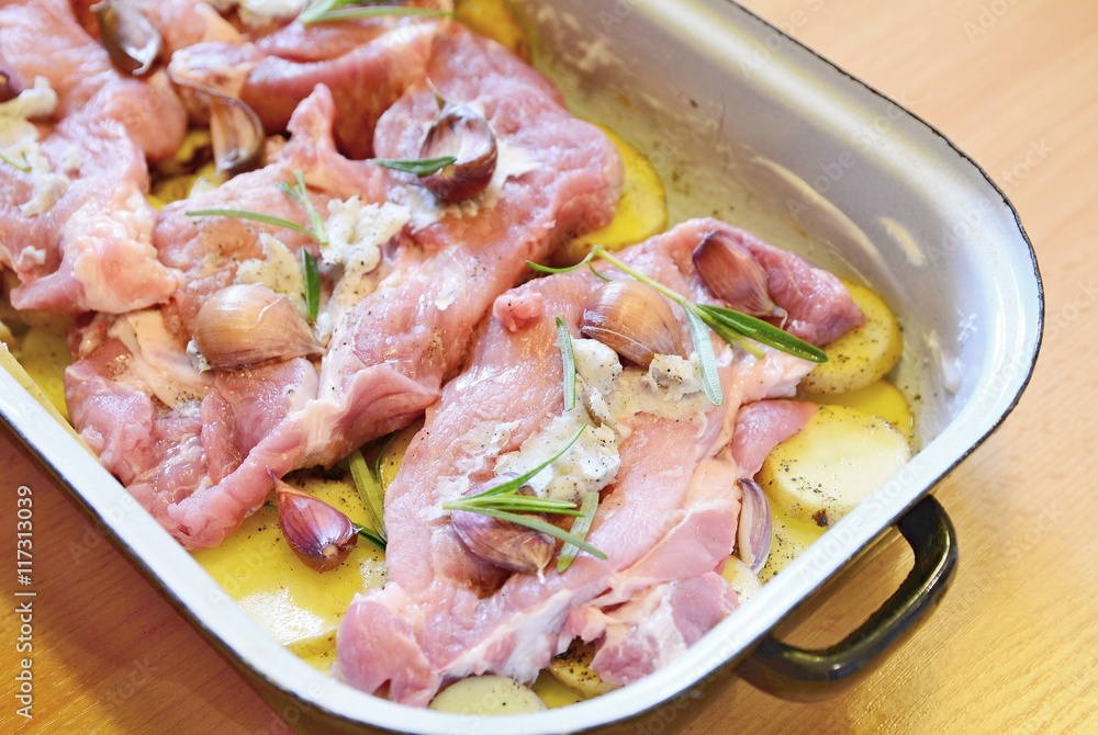 Raw pork neck chops with potatoes slices, rosemary and garlic in pan. The meal is prepared for baking.