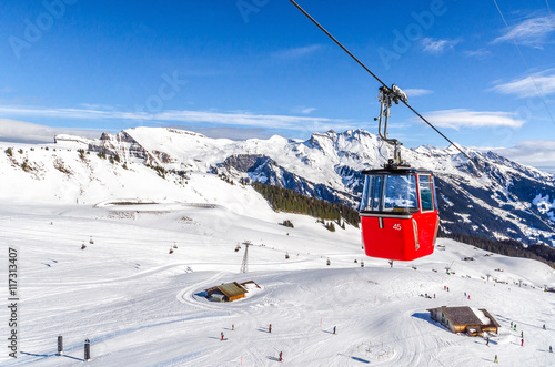 ski slope in Swiss Alps in sunny day. Red cable car above and mountains behind, skiing resort, Switzerland.