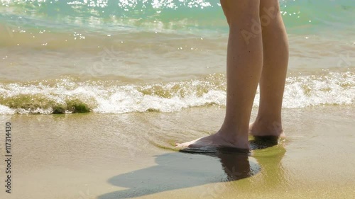 A female is standing on the wet sand close to the waves at the beach. Cold water mixed with sand gives both warmth and coolness. Sunny bright day.