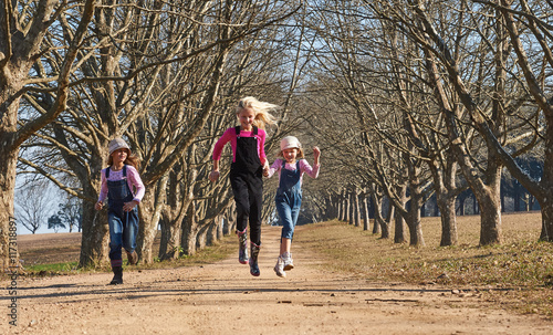 Three girls sisters running skipping down dirt road tree lined a