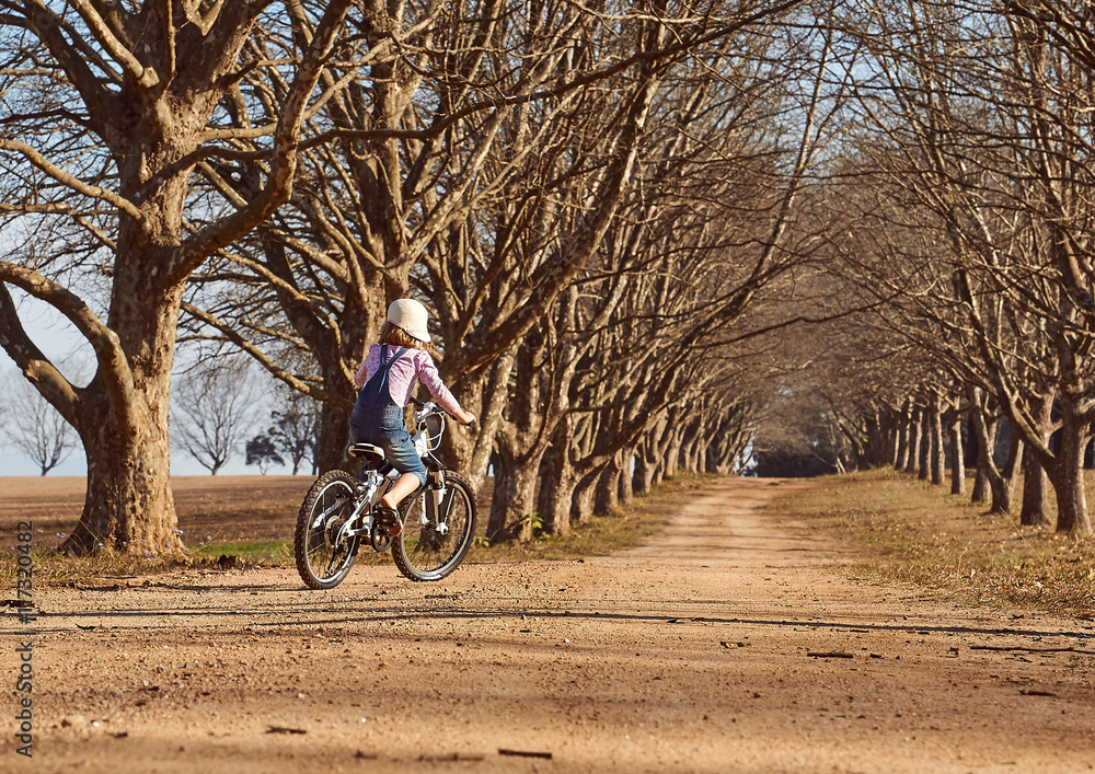 Young girl riding her bicycle bike down dirt road tree lined ave