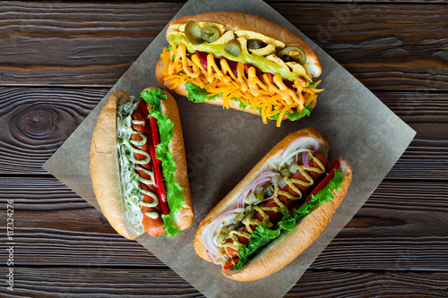 Assorted three hot dogs with ketchup, mustard and salad on a wooden background