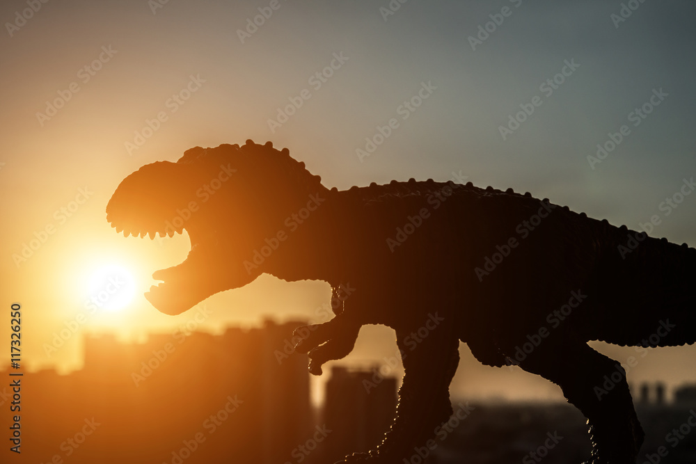 Naklejka premium sylwetka tyranozaura i budynków w czasie zachodu słońca