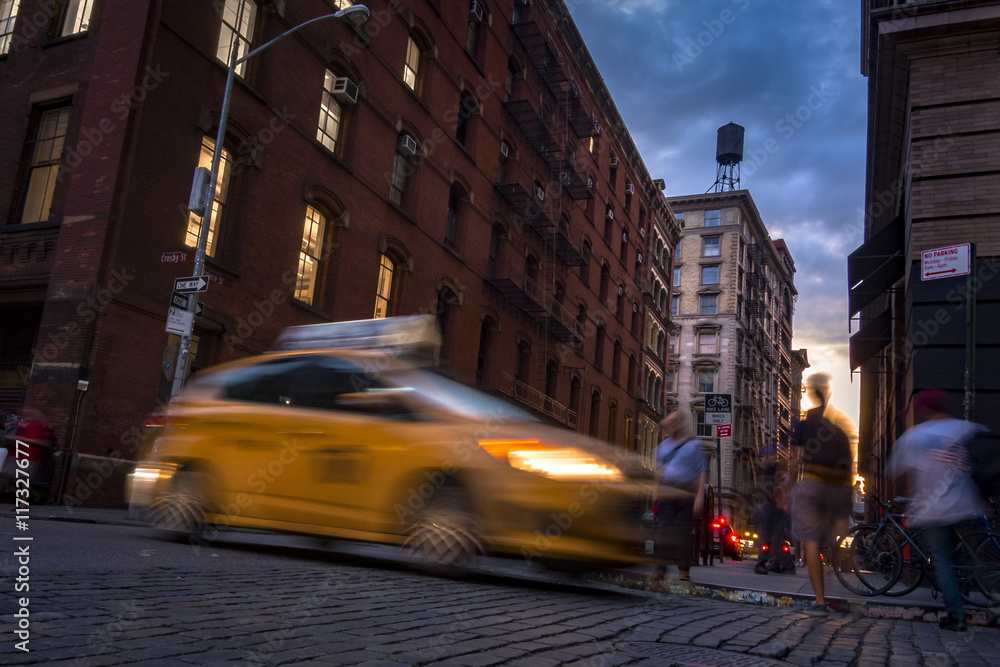Obraz premium Busy street in SOHO, New York, USA with blurry people moving around and a taxi cab at sunset