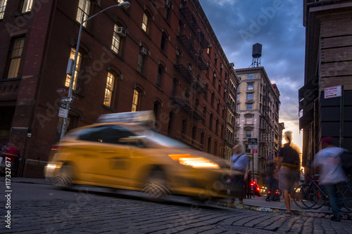 Busy street in SOHO, New York, USA with blurry people moving around and a taxi cab at sunset
