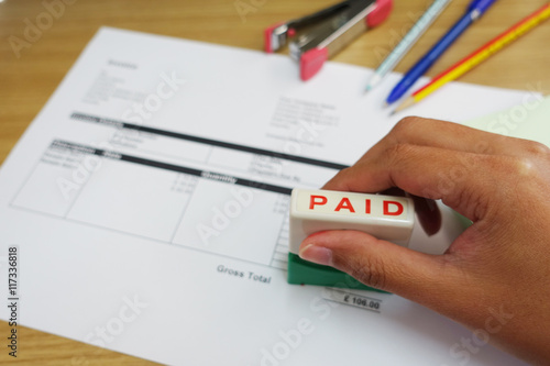  Person Hand Holding Rubber Stamp Over Red Paid Stamp On Invoice 