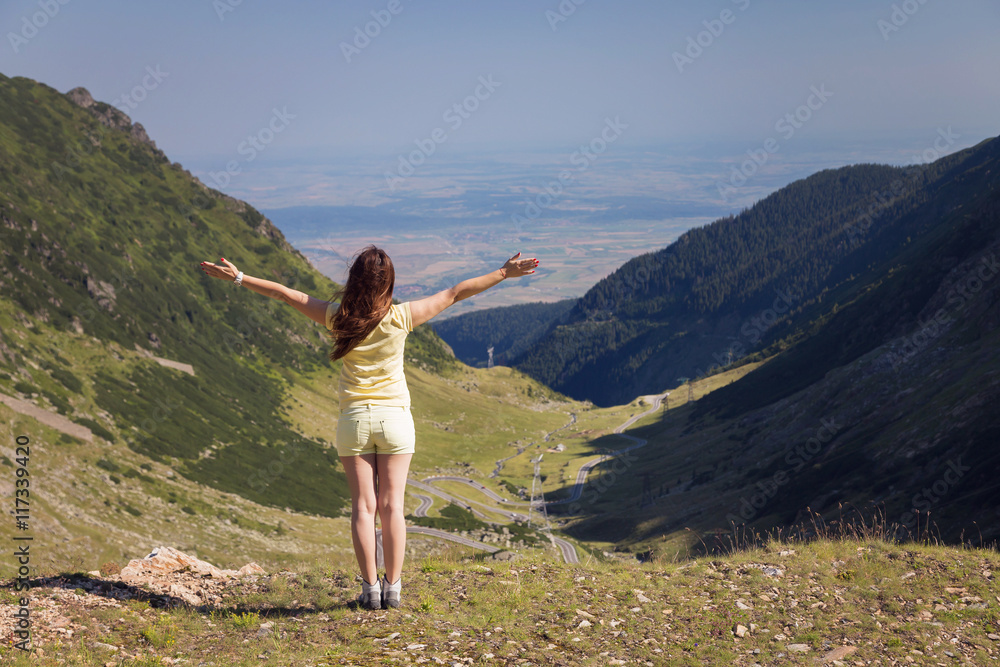 Trekking woman on the peak of Fagaras Mountains, above Transfagarasan highway. Young woman standing on a mountain top with outstretched arms. Vintage look