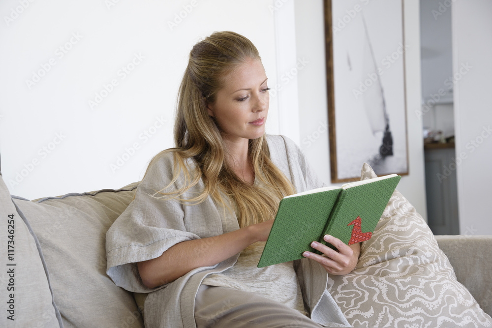 Beautiful woman reading a book while sitting on sofa Beautiful woman reading a book while sitting on sofa