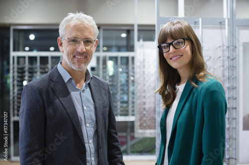 Portrait of shop assistant with customer smiling in optical shop