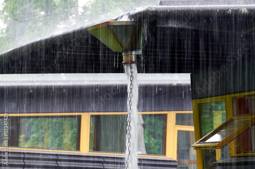 Heavy rain ends from a roof in a big reservoir from where it pour out and down a chain made of metal rings