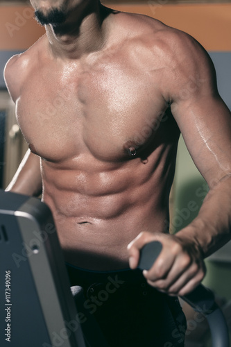 Quadro su tela Young man exercising in the gym on the elipsoid stepper