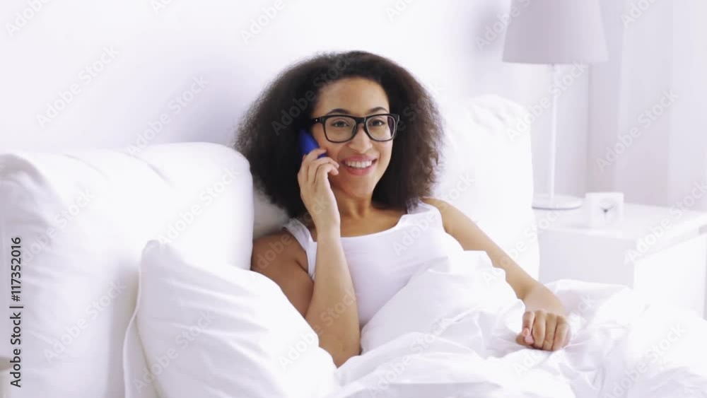african woman calling on smartphone in bed at home african woman calling on smartphone in bed at home