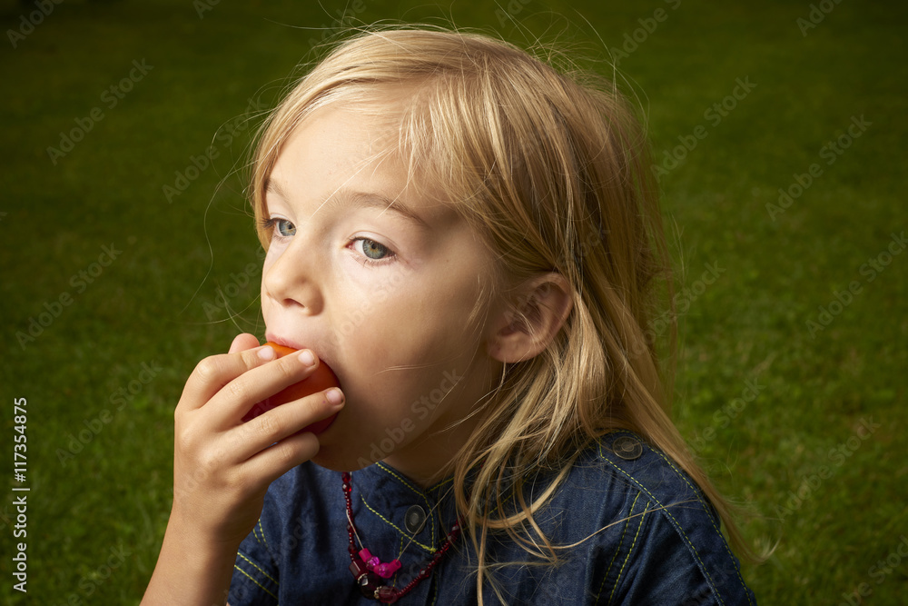 Cute blond child girl eating tomato outside in the garden Cute blond child girl eating tomato outside in the garden