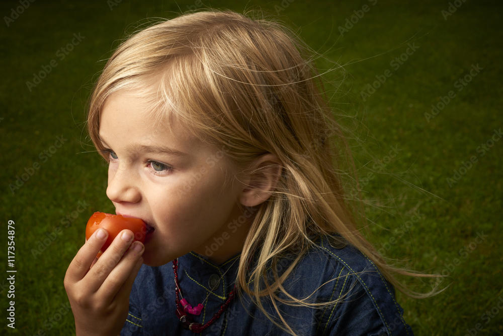 Cute blond child girl eating tomato outside in the garden Cute blond child girl eating tomato outside in the garden