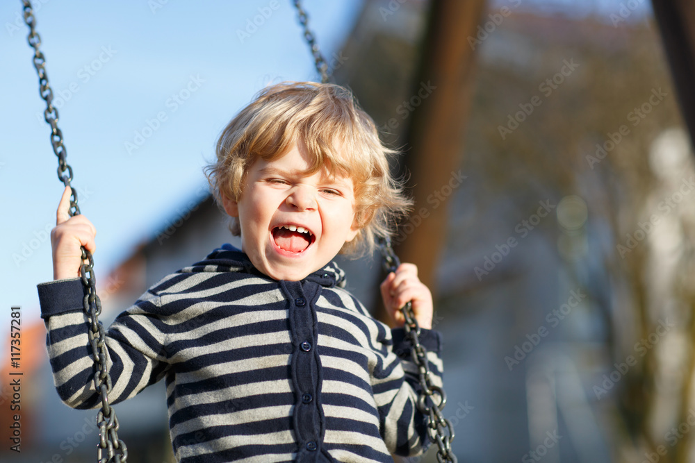 Adorable toddler boy having fun chain swing on outdoor playgroun Adorable toddler boy having fun chain swing on outdoor playgroun
