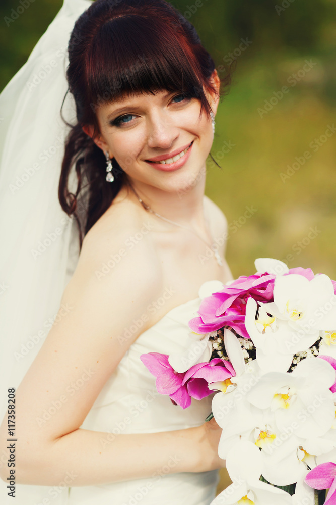 Stunning brunette bride poses on the field holding a wedding bou Stunning brunette bride poses on the field holding a wedding bou