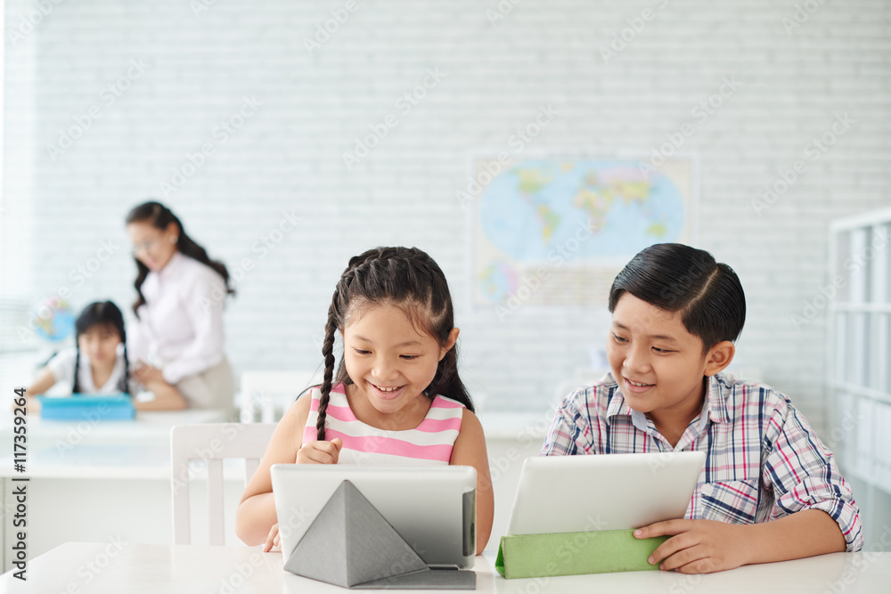 Little classmates using applications on tablet computers