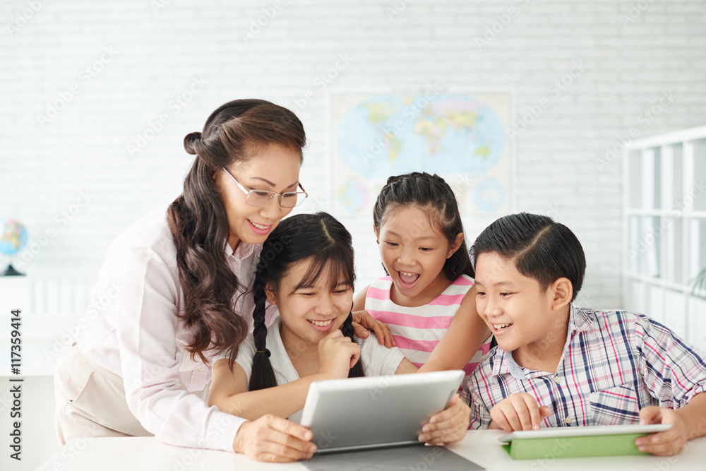 Pupils and their mature teacher watching something on tablet Pupils and their mature teacher watching something on tablet