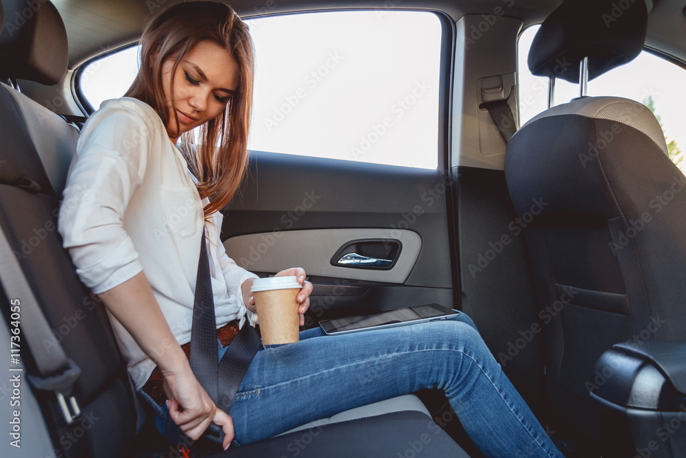 Young, beautiful woman fastens a seat belt, sitting in the back seat of the car