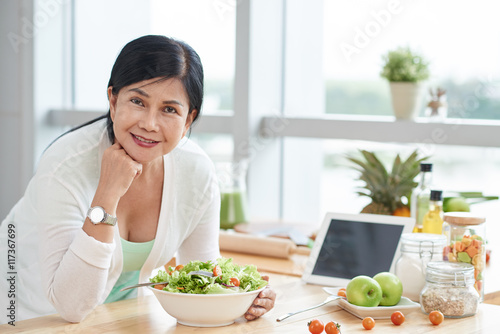 Cheerful Asian woman eating salad at home