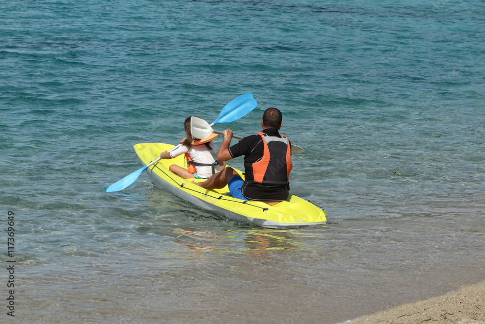 Daughter and father exploring calm tropical bay by kayak. Back view.