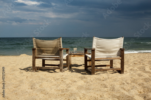 Seaside view with two chairs and table with an empty glass on it