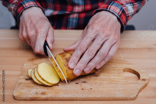 Man hands slicing fresh potato by ceramic knife