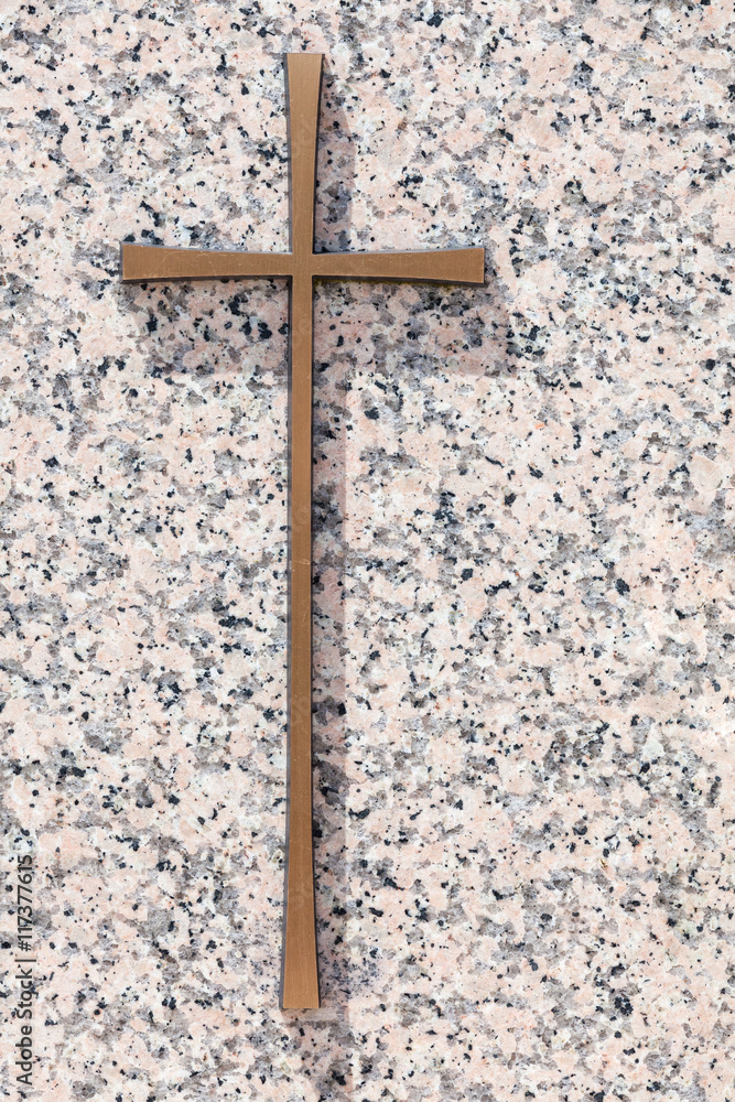 A simple gold memorial cross on a polished light pink granite slab with copy space for a funeral or religious message A simple gold memorial cross on a polished light pink granite slab with copy space for a funeral or religious message