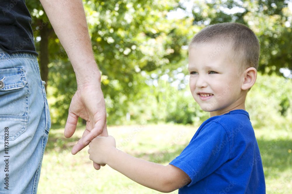 father and son holding hands walking in the summer park father and son holding hands walking in the summer park