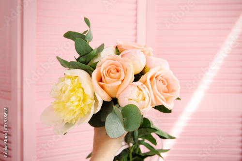 Hand holding bouquet of flowers on pink screen background