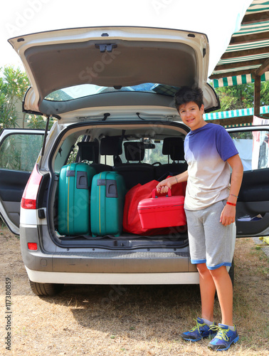 boy loads a little red suitcase in the trunk