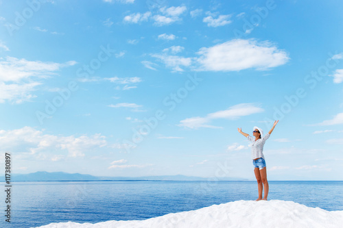 Young woman standing on white beach with her arms outstretched over horizon. She is looking towards the sun.