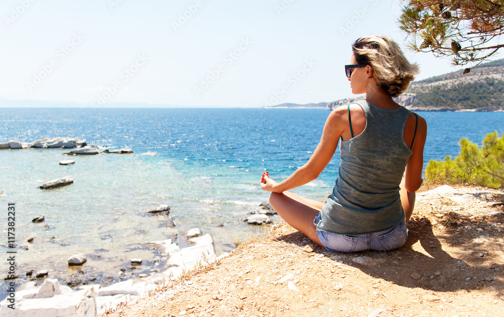 Young woman sitting on sea cliff in lotus position Young woman sitting on sea cliff in lotus position