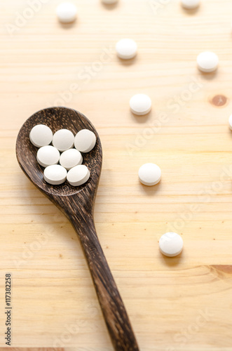 medicine tablets and wooden spoon on wood background