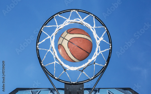 Basketball falling through the net. Blue sky on the background. photo