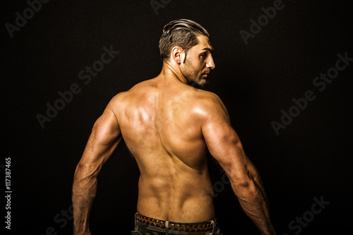 Quadro su tela Rear view of a muscular young man with a bare torso, black background