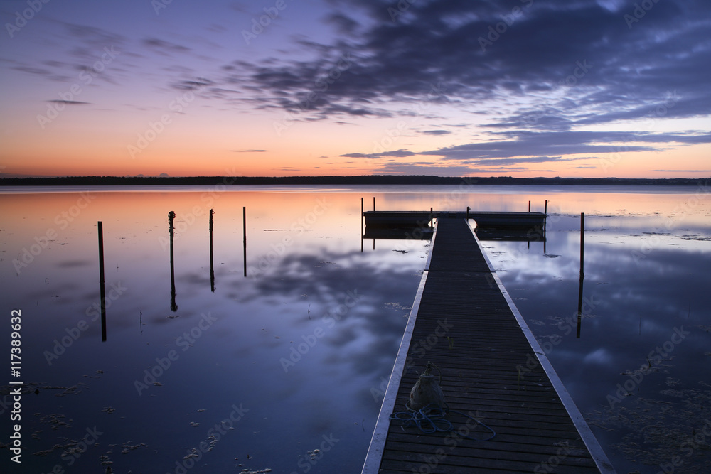 Fototapeta premium Drewniane molo na spokojnym jeziorze o wschodzie słońca