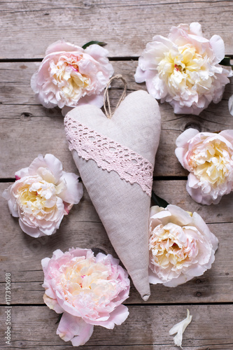 Decorative heart and  pink peonies flowers on aged wooden background. Flat lay.  Selective focus.