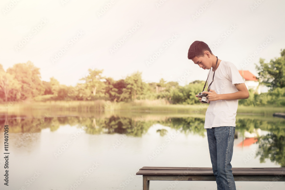 Young photographer sitting on the wooden deck beside the water with sunrise. Young photographer sitting on the wooden deck beside the water with sunrise.