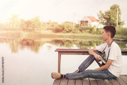 Young photographer sitting on the wooden deck beside the water with sunrise.
