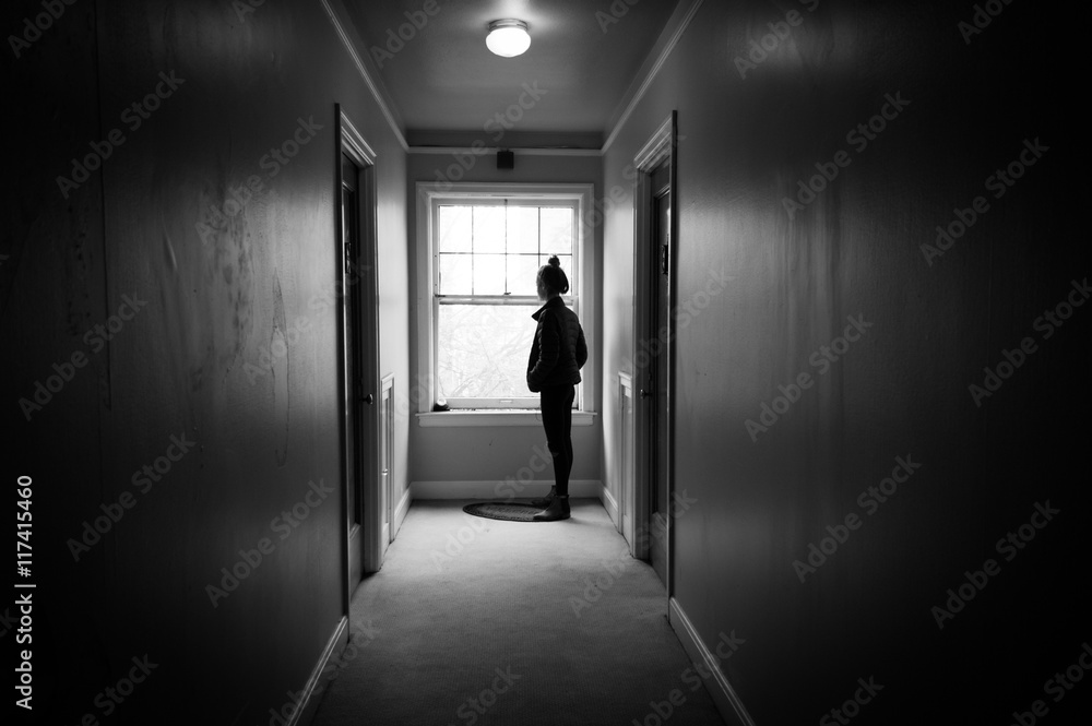 Young woman in a dark hallway looking out a window.