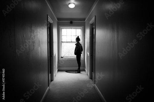 Young woman in a dark hallway looking out a window.
