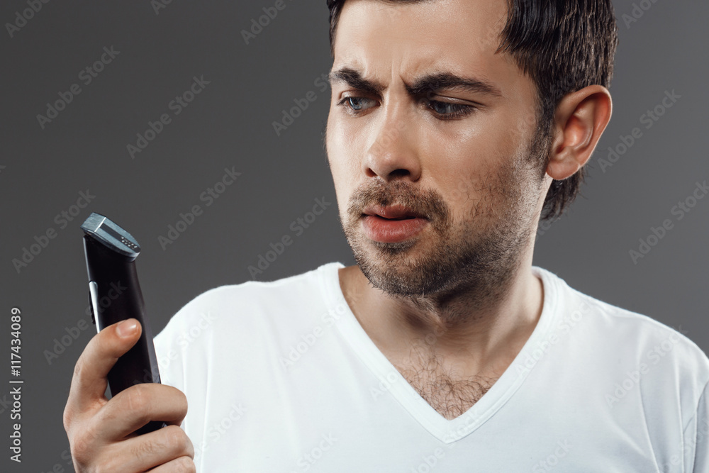 Young handsome man shaving over grey background. Young handsome man shaving over grey background.