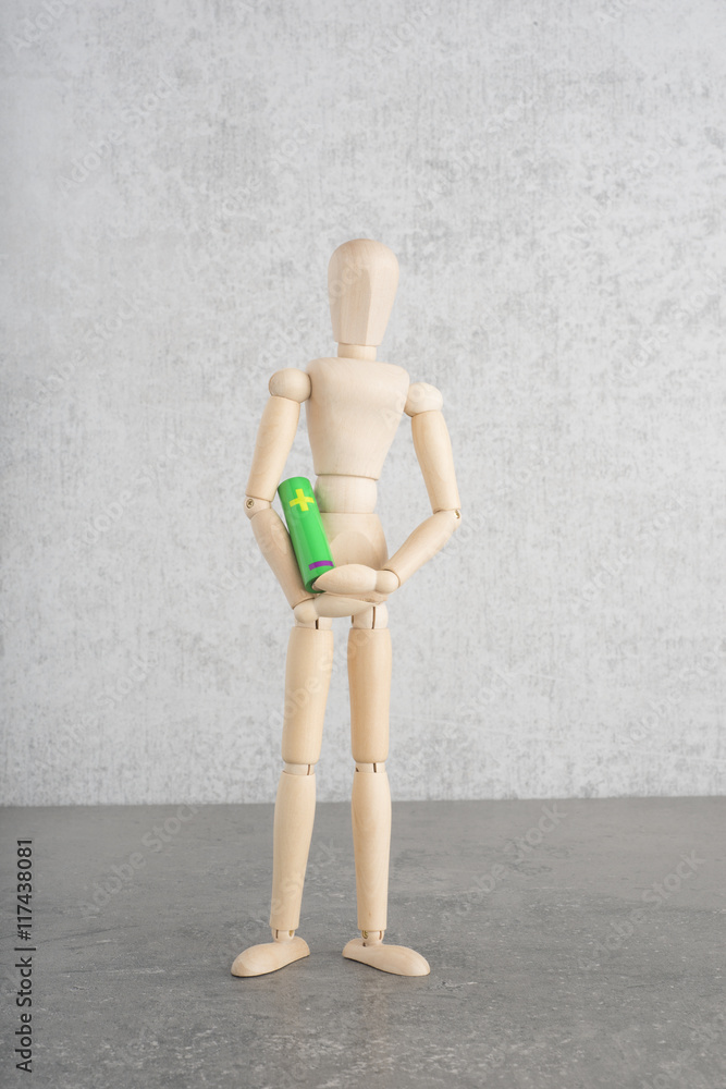 Concept of green energy and power with wooden figure holding aa alkaline battery. Symbol of environmental friendly electricity and green lifestyle. Concept of green energy and power with wooden figure holding aa alkaline battery. Symbol of environmental friendly electricity and green lifestyle.