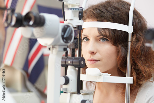 Pretty woman is looking into eye test machine with concentration in oculist lab