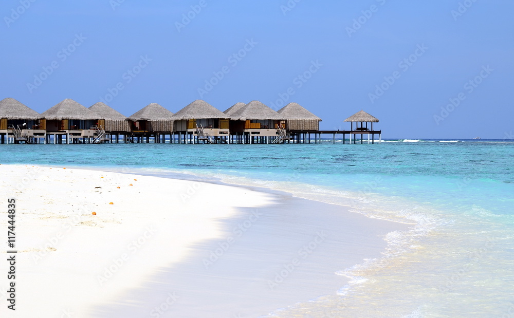 Maldivian beach with white sand, azure water and wooden villas