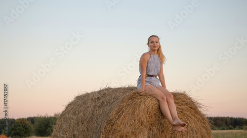 Beautiful young girl resting at stacks of hay at sunset