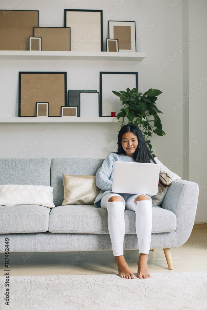Smiling young woman sitting on couch at home using laptop Smiling young woman sitting on couch at home using laptop