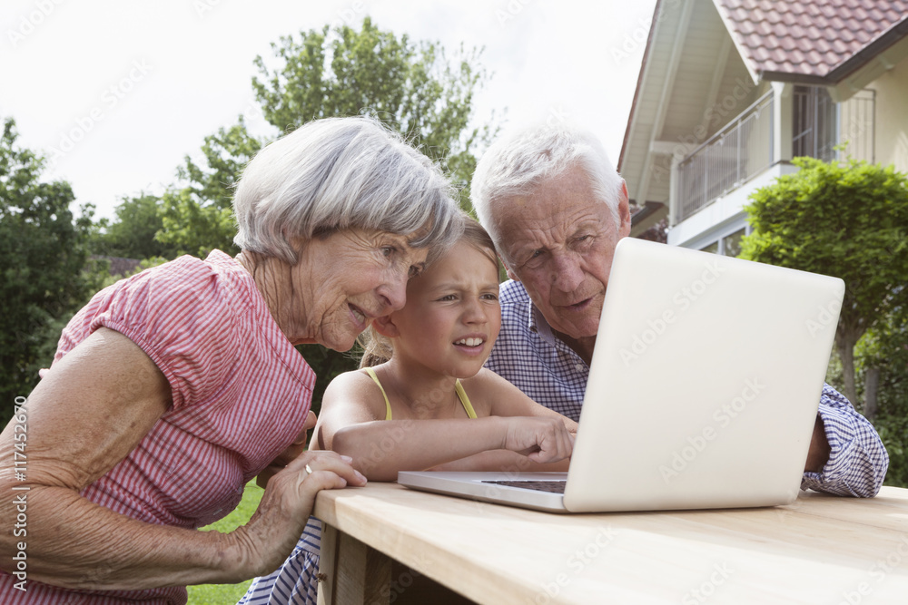 Grandparents and granddaughter using laptop in garden Grandparents and granddaughter using laptop in garden